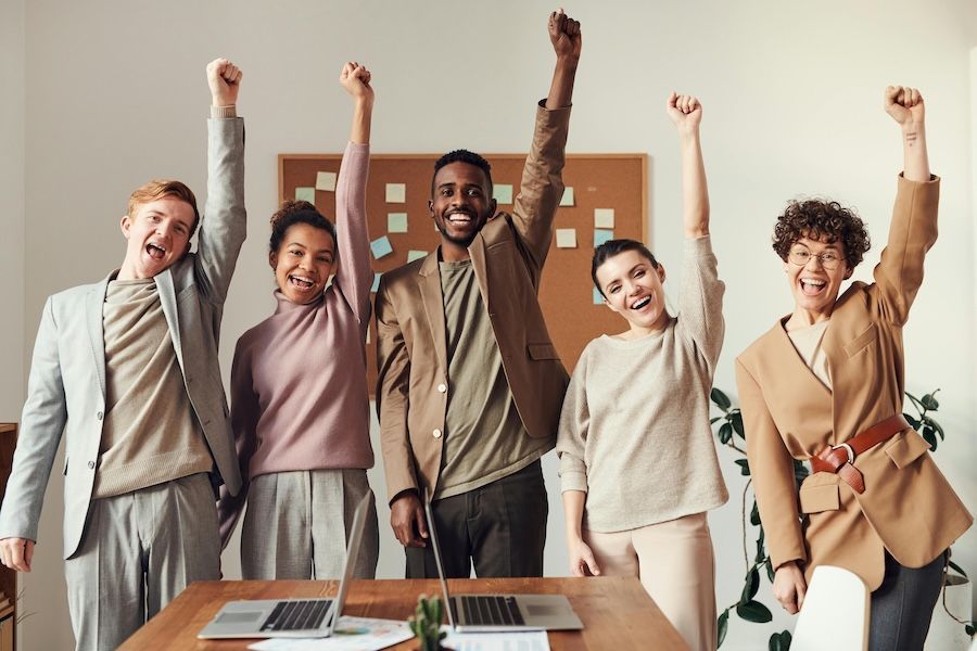 group of smiling people rising their left arm up in an office space