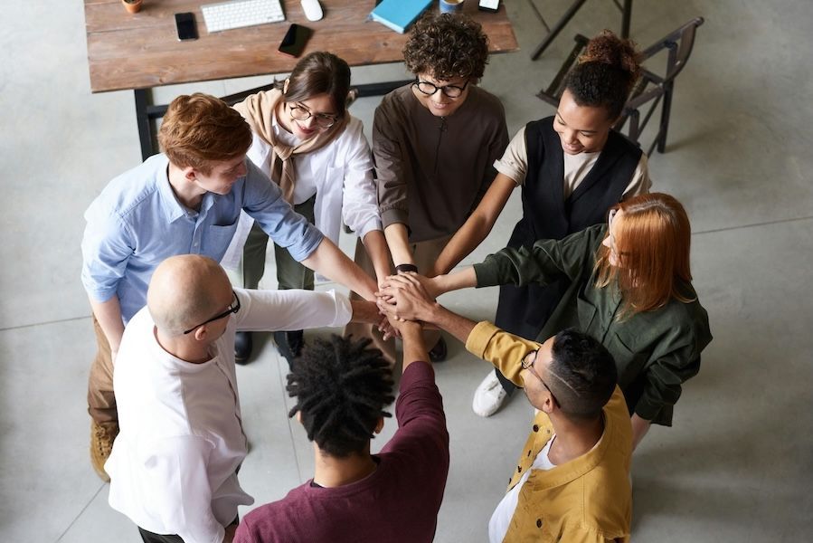 team of people in an office space, gathering their hands together 
