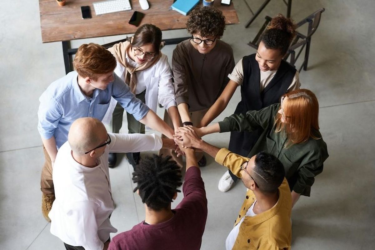 team of people in an office space, gathering their hands together